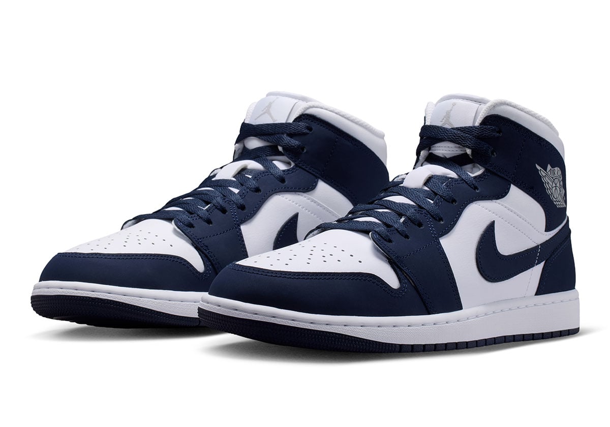 Front three-quarter pair shot of the white and navy Air Jordan 1 Mid Obsidian with grey Wings logos on the ankles