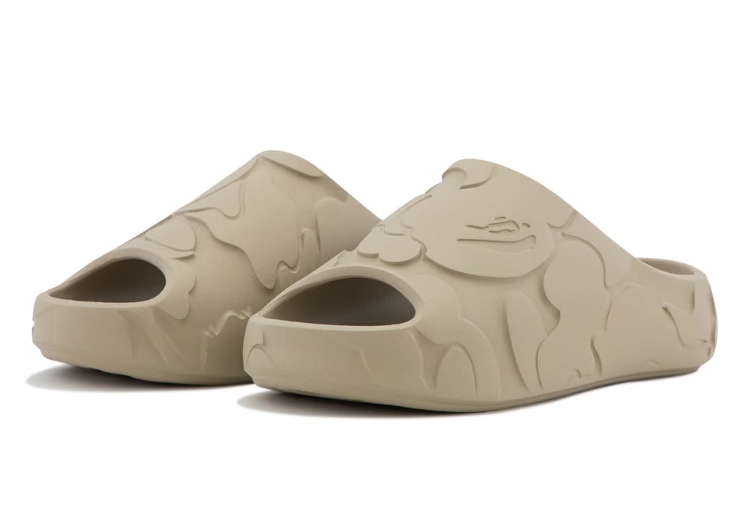 Front three-quarter look at the beige BAPE Slide with the molded camo upper and tonal ape head on the strap