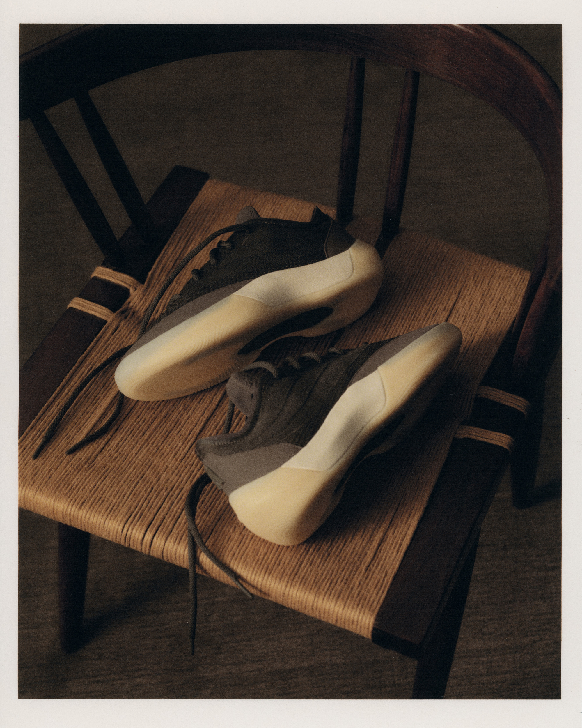 Pair of the Fear of God Athletics III Basketball "Cinder" resting on a woven-seat wooden chair