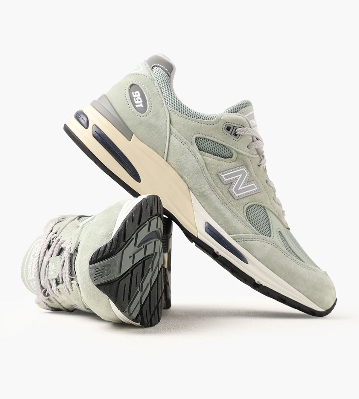 Styled shot of the sage-green Made in UK 991v2 leaning against a second pair turned to show the tread