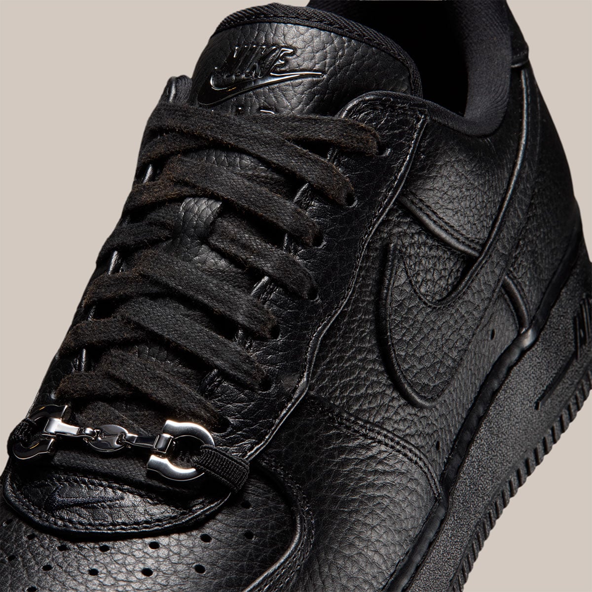 Macro detail of the silver horsebit loafer-buckle accent and chrome NIKE tongue plate on the black Air Force 1