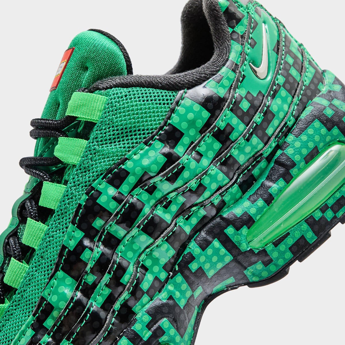 Macro detail of the silver Swoosh and pixelated dot-and-brick print across the layered green Air Max 95 side panel