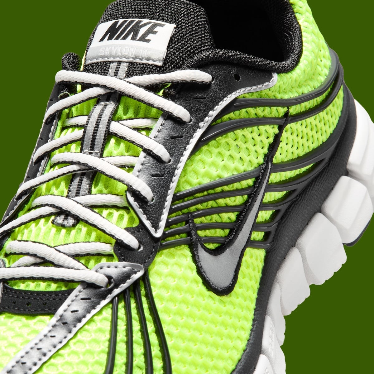 Close-up of the black ribbon cage fanning across the volt mesh toe with white laces and a NIKE tongue tab