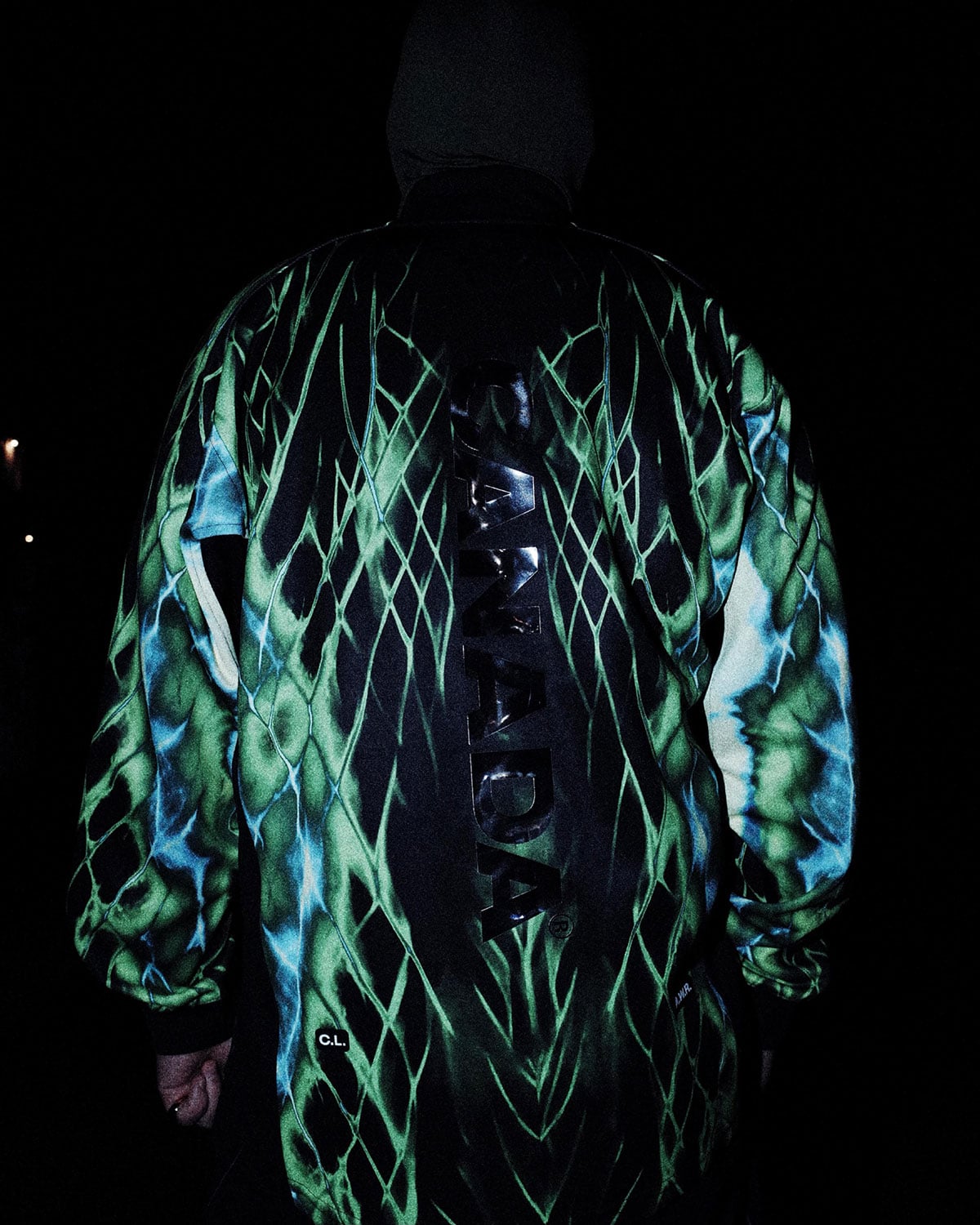 Back of the NOCTA Team Canada track jacket with a green and blue northern-lights print and raised CANADA text