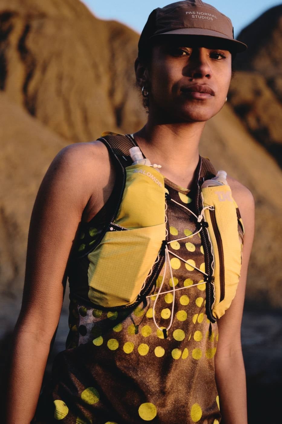 Runner wearing the yellow Pas Normal Studios x Salomon RACE SKIN 2 vest with front hydration flasks at golden hour