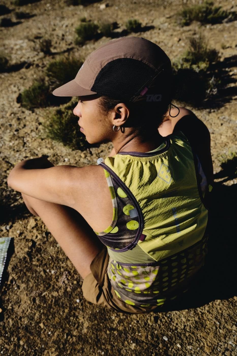 Seated runner in the T.K.O. cap and green-and-yellow polka-dot Pas Normal Studios running kit on desert terrain