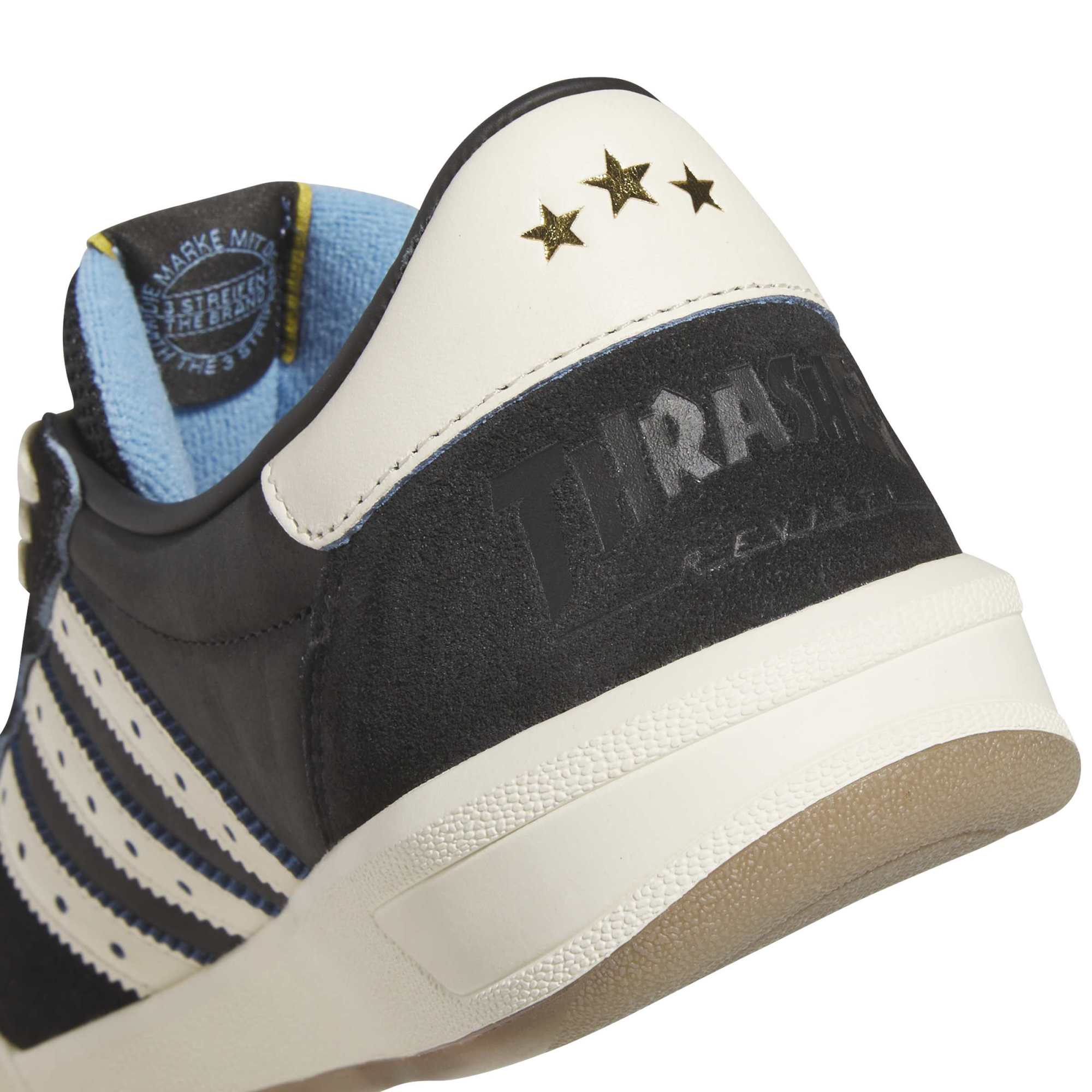 Macro detail of the three gold stars and debossed Thrasher Revista logo on the black suede heel