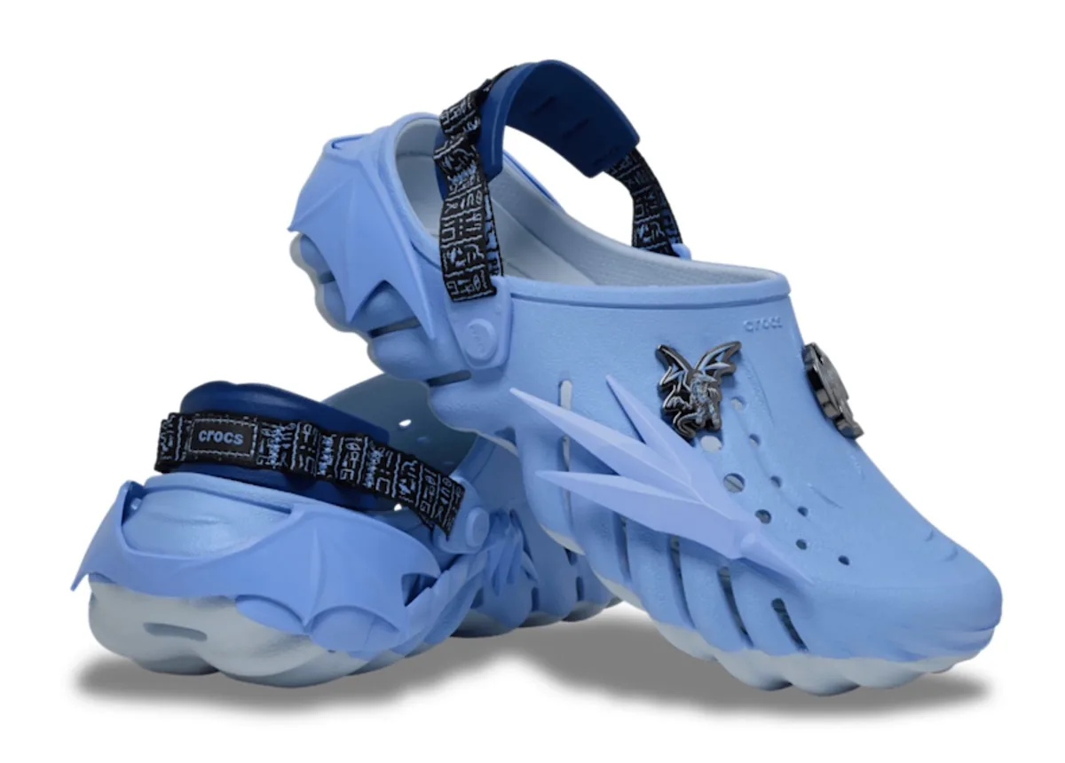 angled pair, pale blue spiky clogs with dragon charms and navy hieroglyph straps, x Crocs Collection