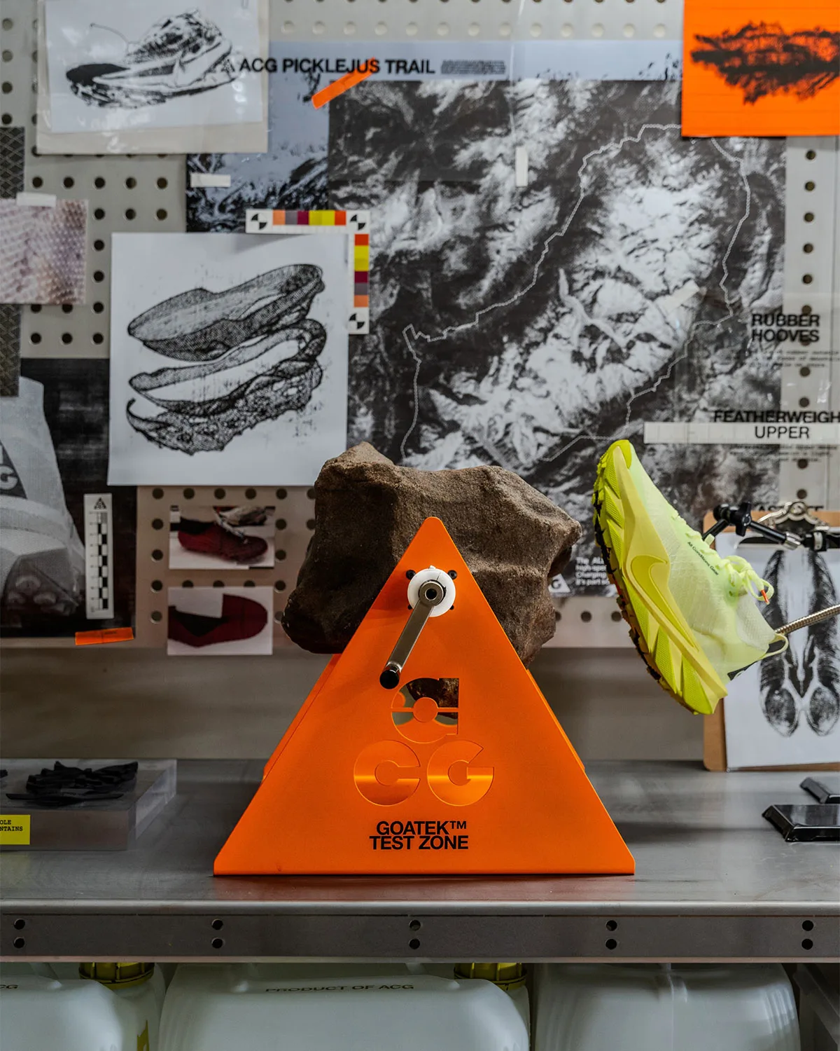 Shoe on display stand beside orange Goatek Test Zone sign and rock, studio backdrop, Nike ACG Picklejus