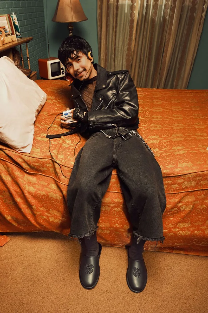 on-foot, man seated on an orange bedspread in a leather jacket wearing black mules, Willy Chavarria Collection
