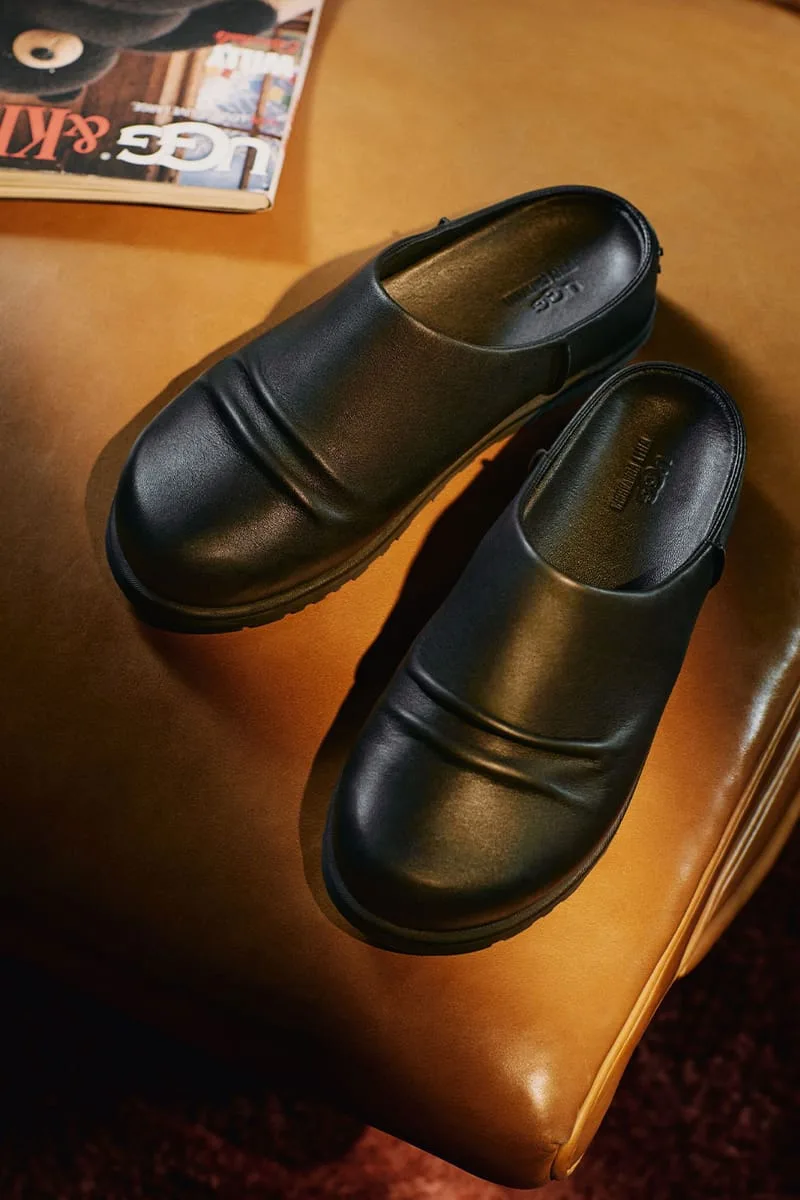 top-down pair of black leather mules on a tan ottoman beside a magazine, Willy Chavarria Collection