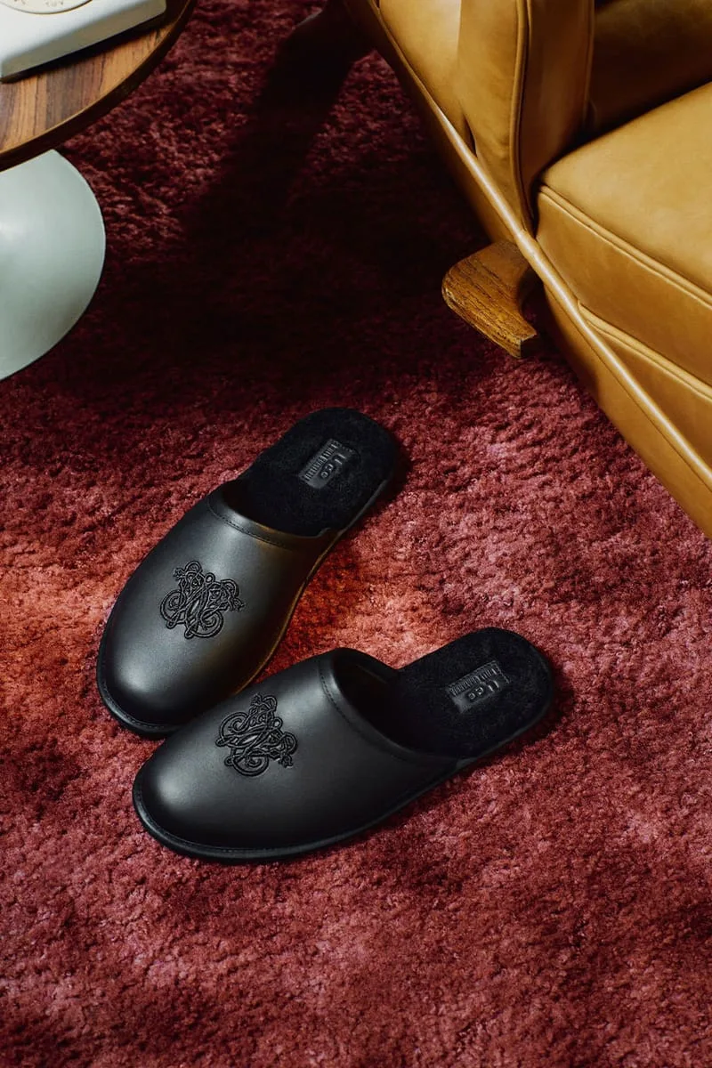 two pairs of black mules on a red shag rug by a leather chair leg, Willy Chavarria Collection