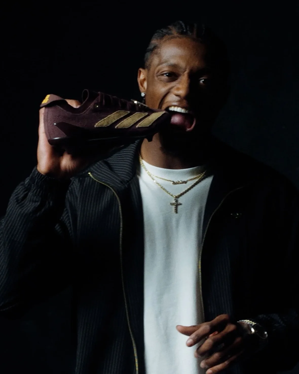 in-hand shot, man biting the tan-striped maroon suede shoe, II x Snickers