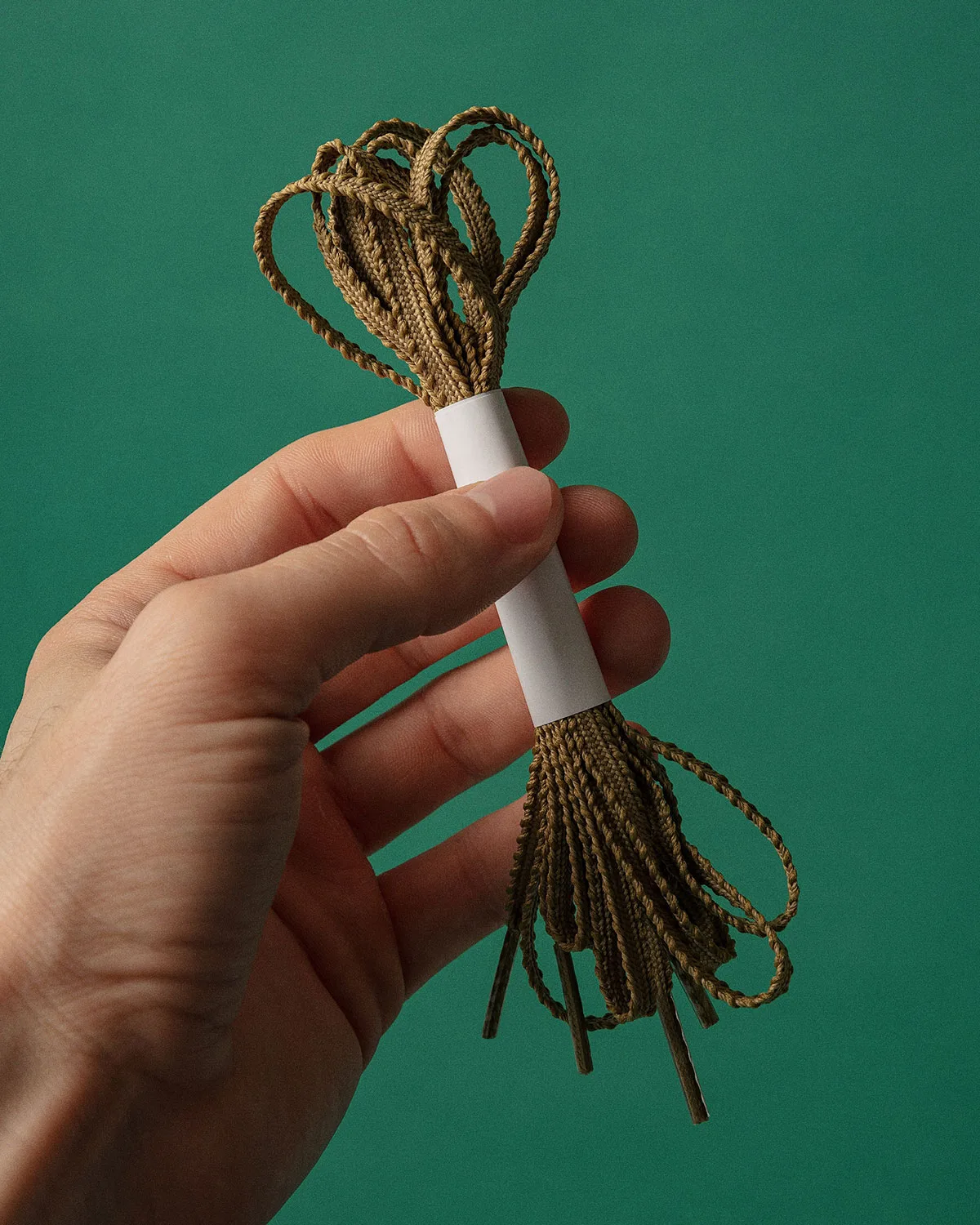 detail of braided olive-brown laces bundled in hand with paper band, x Up There