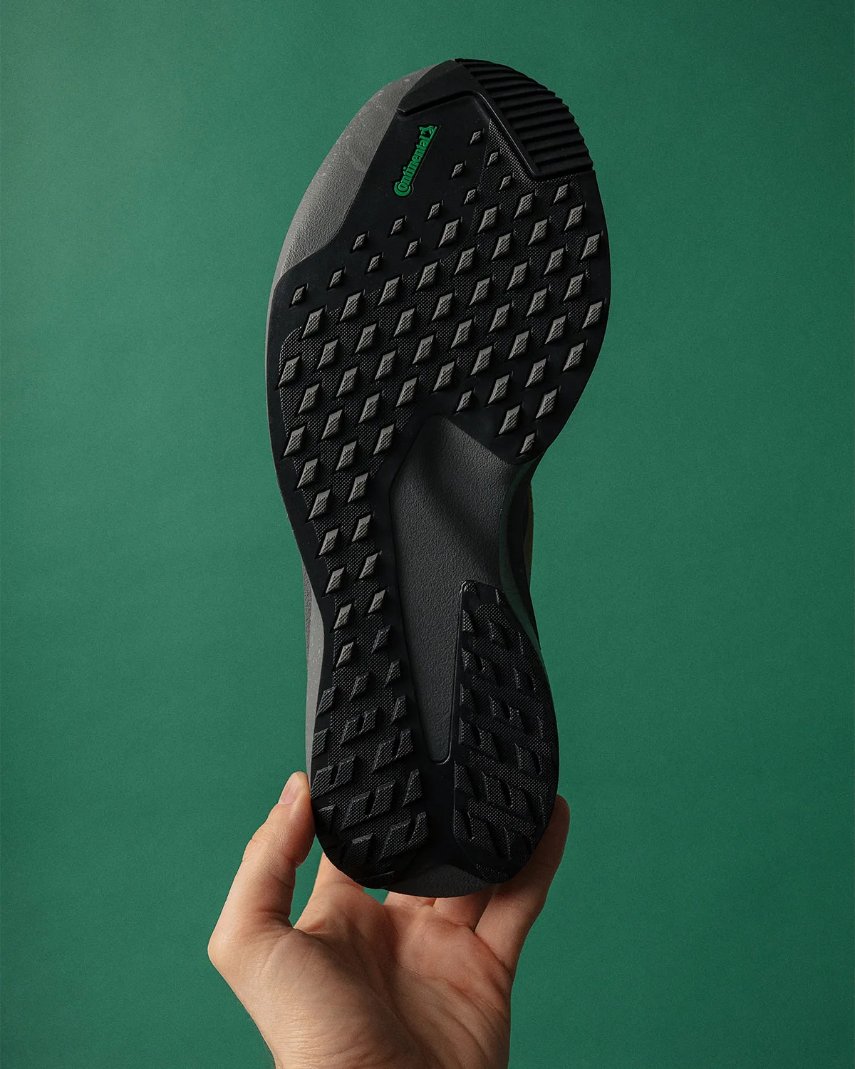 outsole close-up in hand, black lug tread, green Continental logo, x Up There