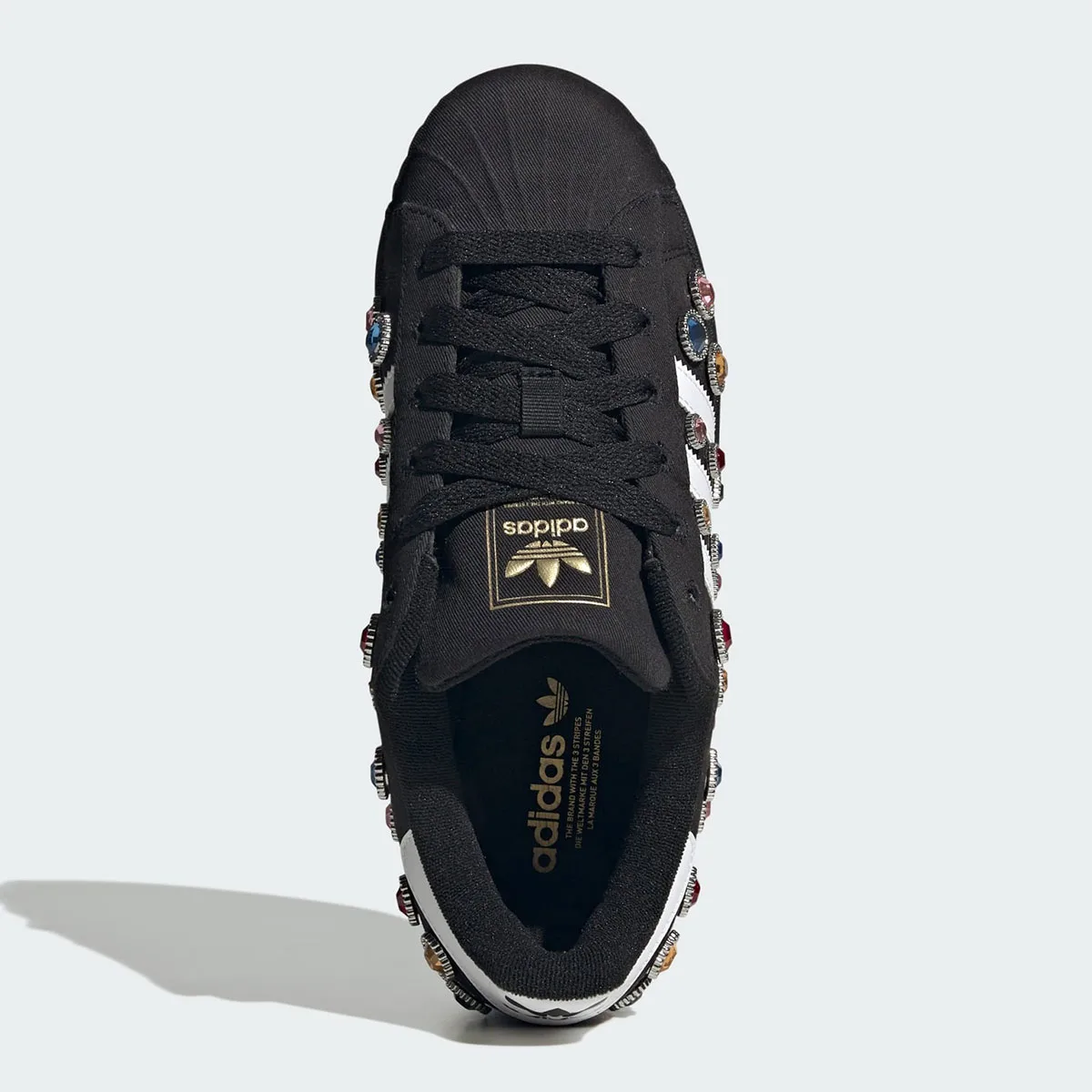 top-down view, jewels lining the lace panel with gold adidas branding on tongue, Jewel