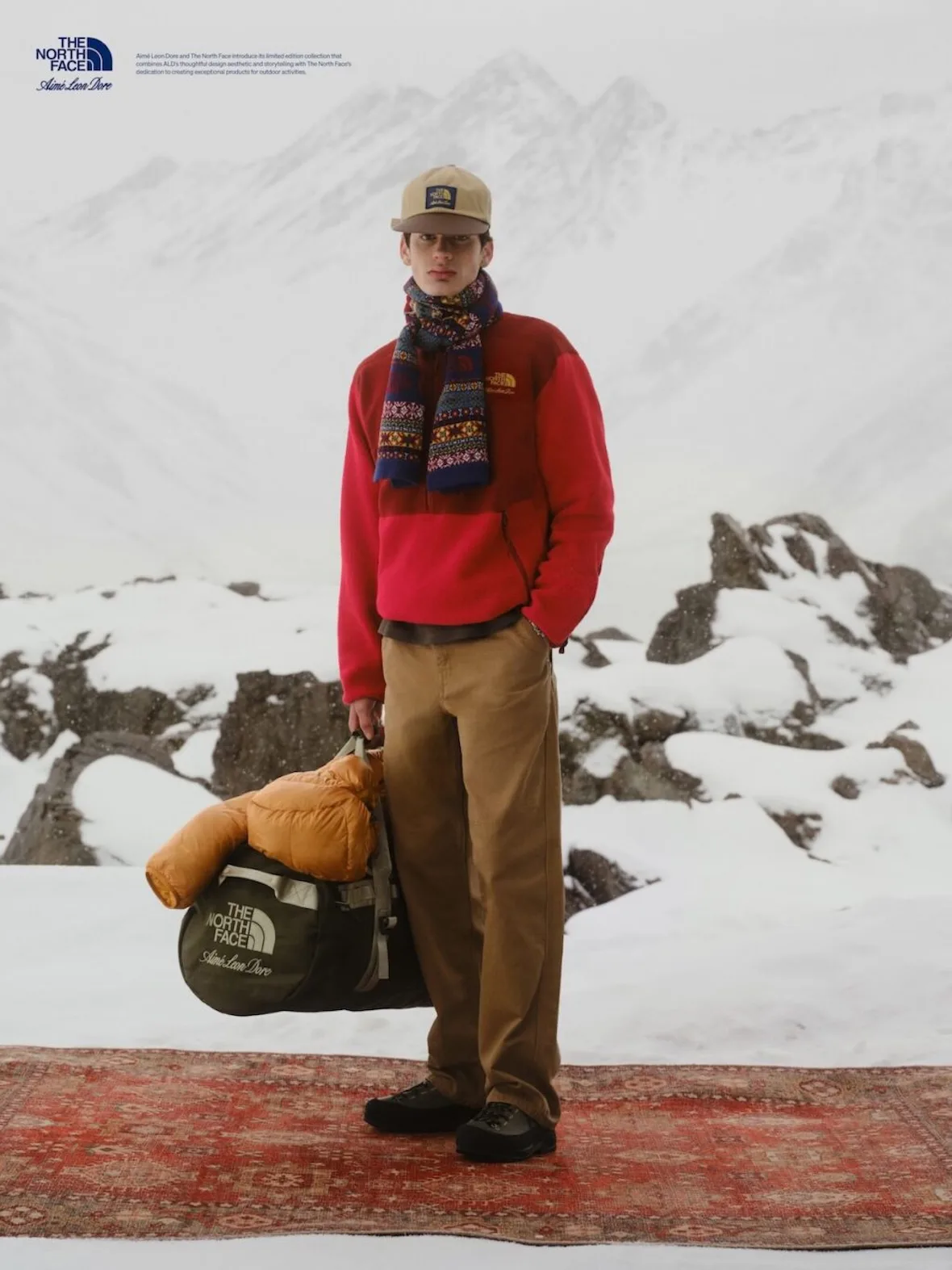 on-foot, red fleece pullover, tan cap and scarf, holding branded duffel bag, Fall/Winter 2026 Collection