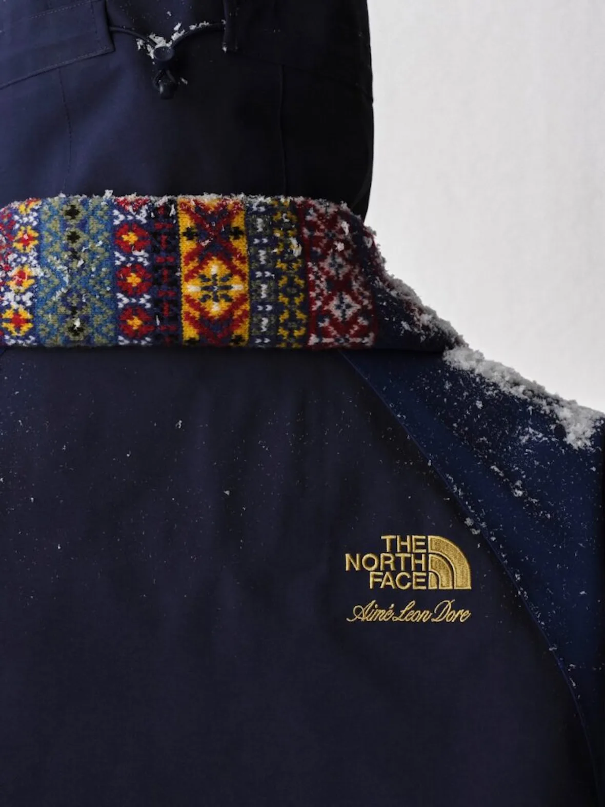 detail, fair isle knit gaiter over navy jacket, snow-dusted shoulder, Fall/Winter 2026 Collection