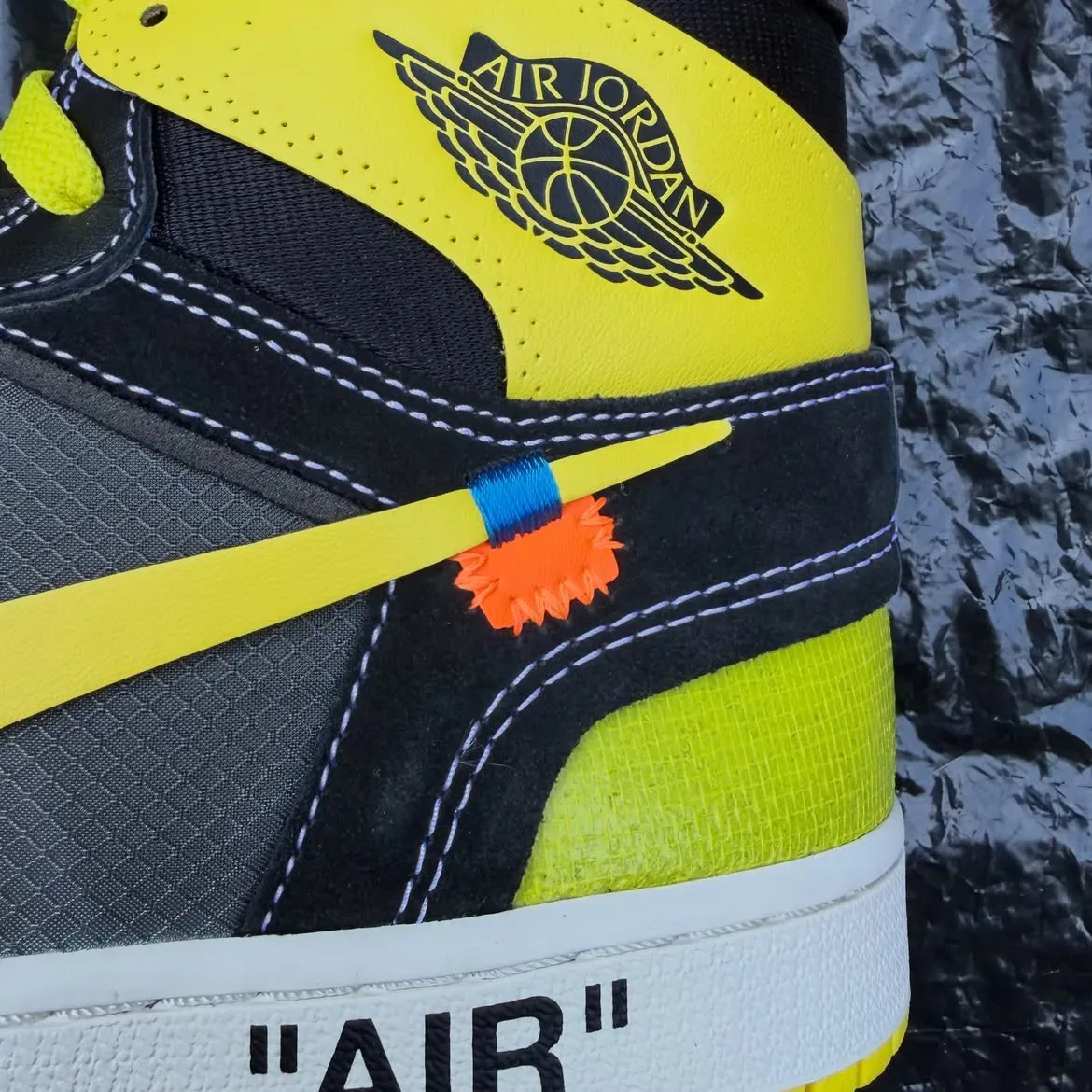 heel detail with yellow Jordan Wings logo and orange zip-tie tag on black suede, Black/Lightning