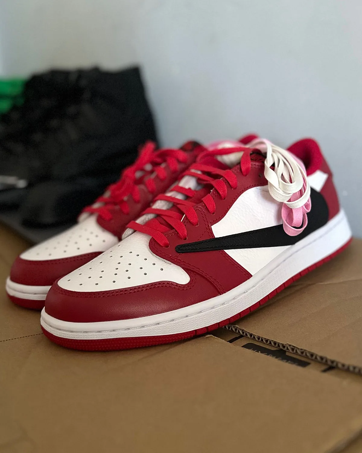 Lateral pair view on cardboard box, red toe box with untied pink and white laces, 1 Low OG