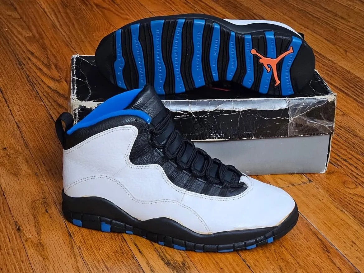 heel-up on wood floor beside torn box, orange Jumpman on blue/black outsole, Knicks