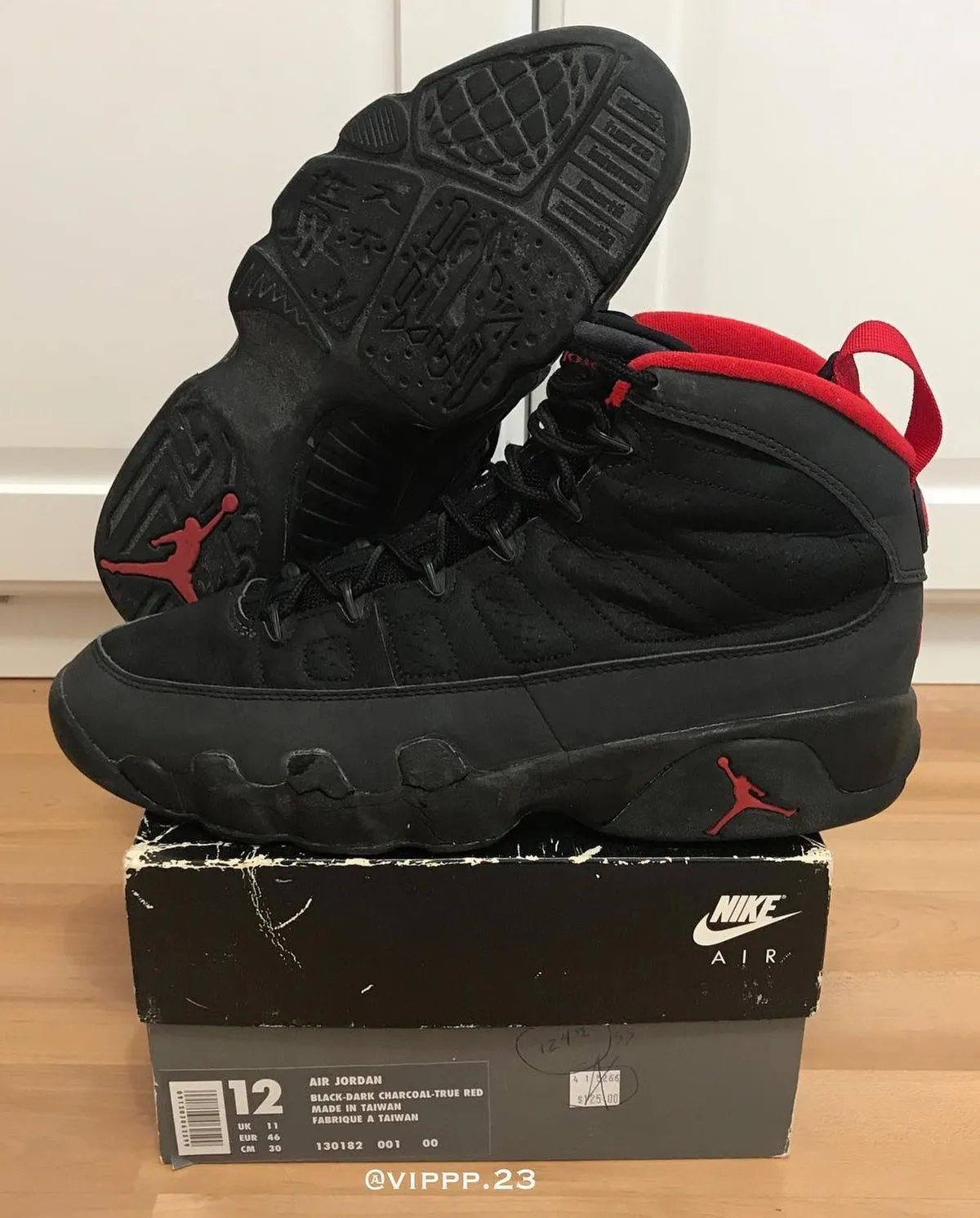 pair perched on worn Nike shoebox, outsole and red collar lining visible, wood floor, Charcoal