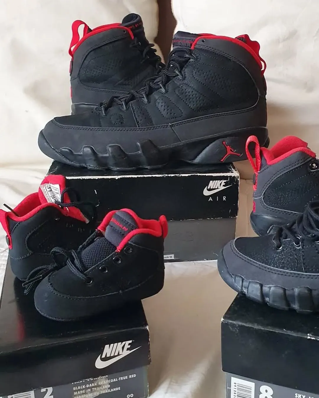 three pairs in adult and toddler sizes on Nike boxes, black with red trim, cream backdrop, Charcoal