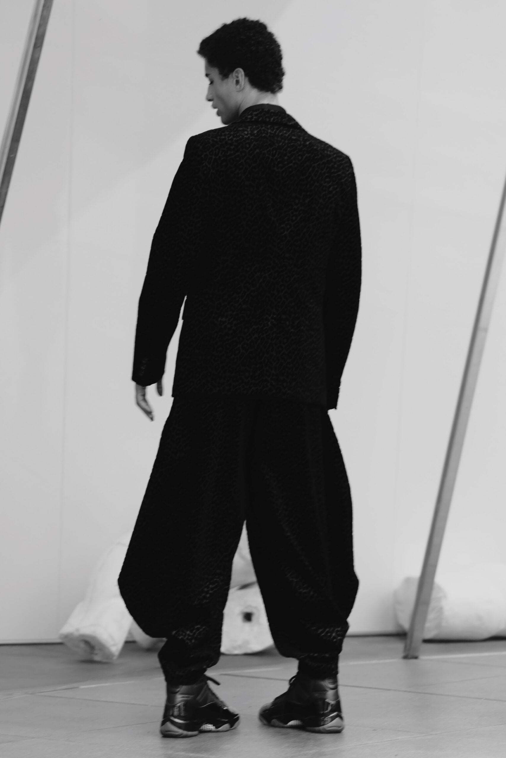 Rear view, model in black leopard-textured suit with black high-top sneakers, Air Jordan 11