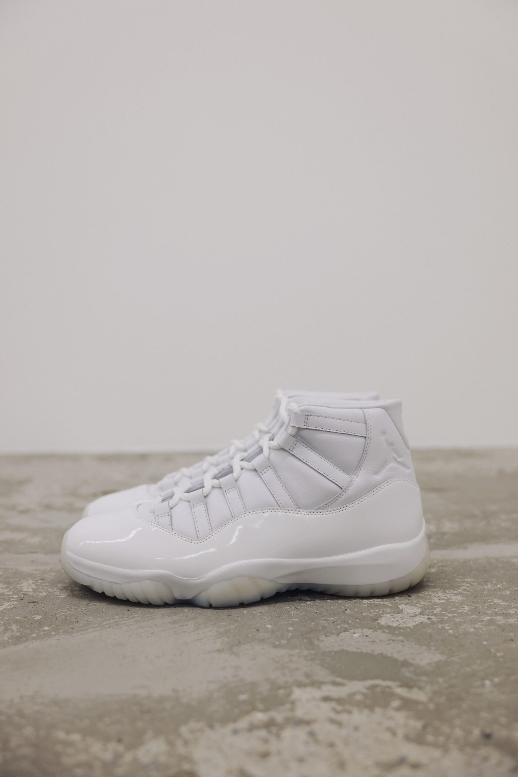 Lateral view, white patent leather high-top sneaker on concrete floor, Air Jordan 11
