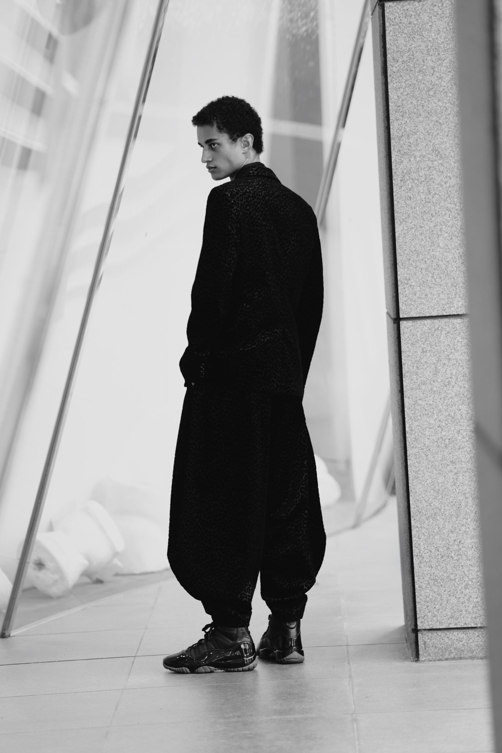 Rear view, model in black leopard-print coat with black high-top sneakers, Air Jordan 11