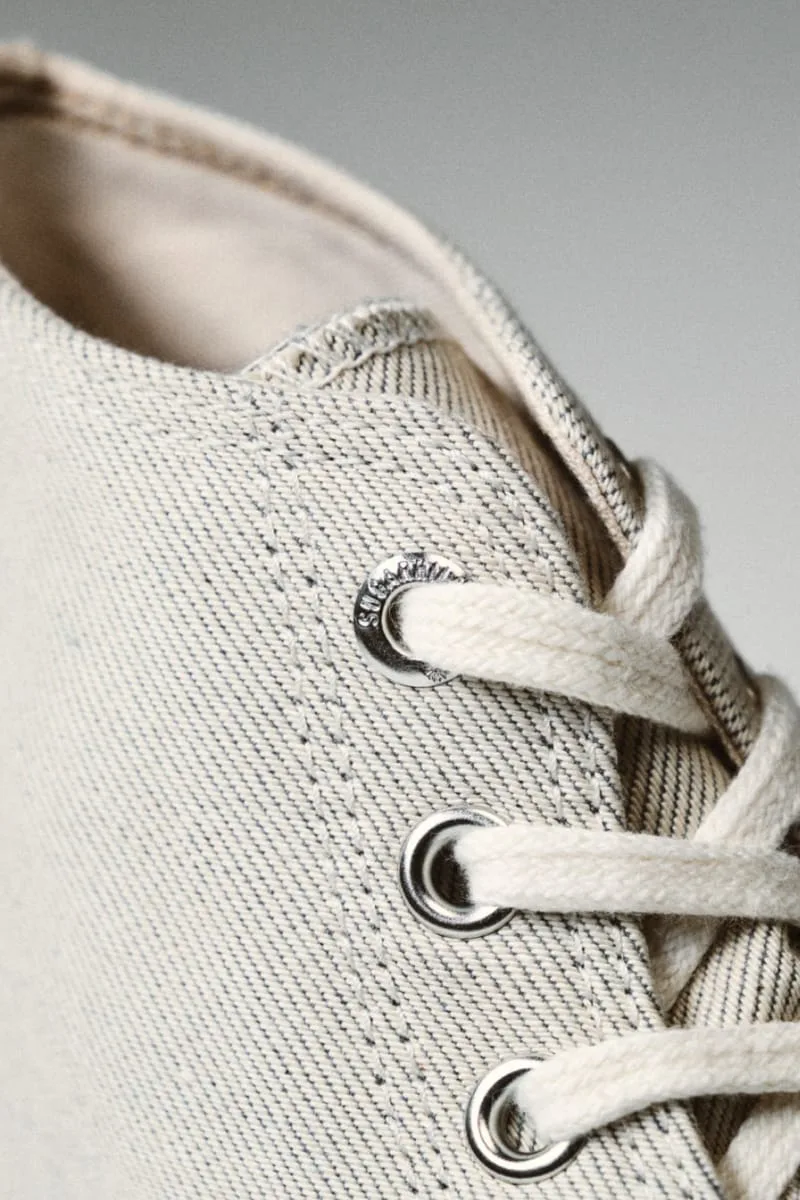 eyelet detail, cream laces through a grommet stamped with brand text, Natural