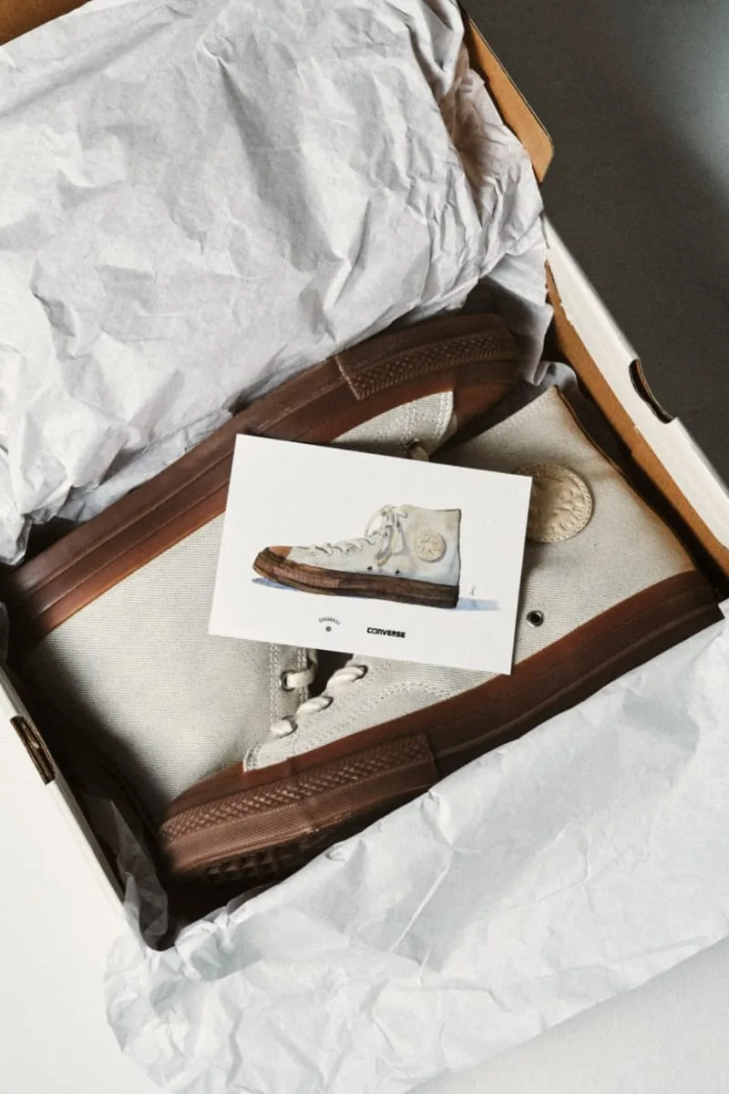 packaging shot, shoe nestled in tissue paper box beside an illustrated card, Natural