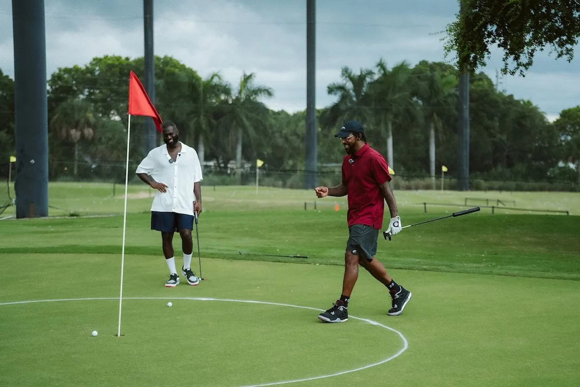 two men on putting green by red flag, one in maroon polo pumping fist, investment, no product)