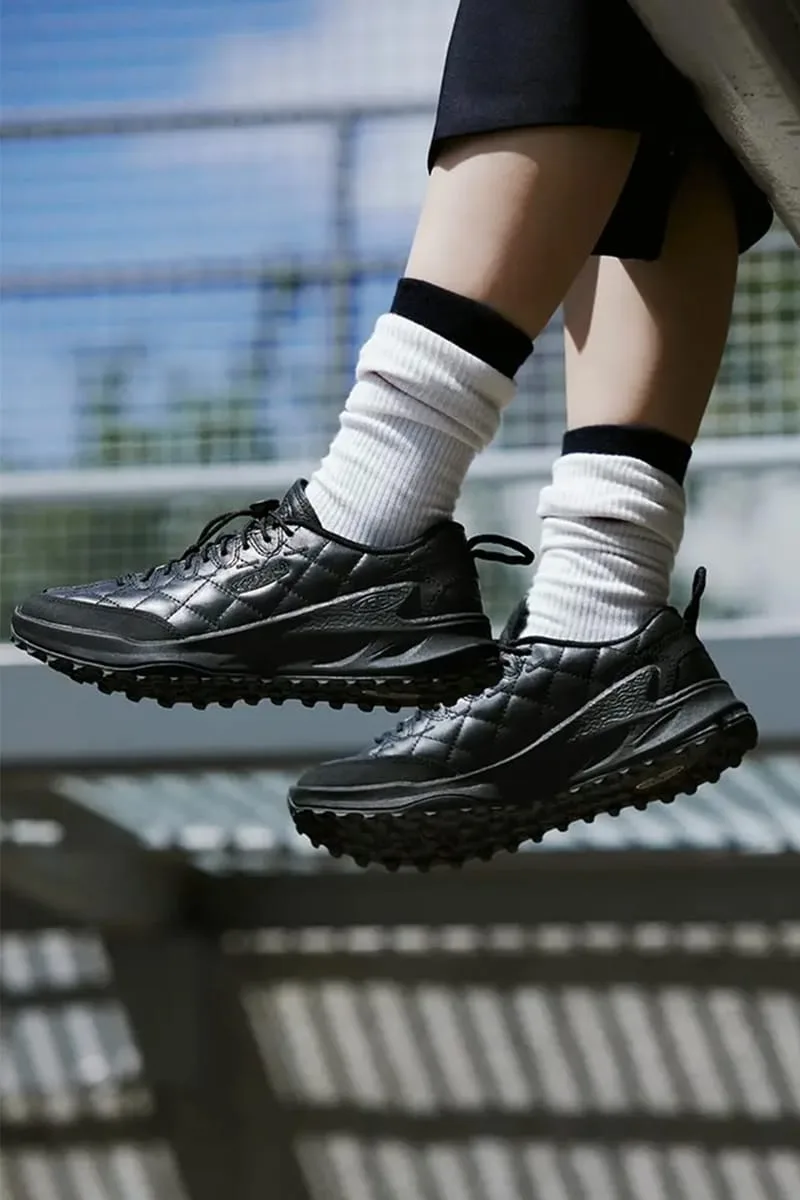 on-foot side view with white ribbed socks, black quilted upper against sky and mesh backdrop, DOE Jasper Zionic