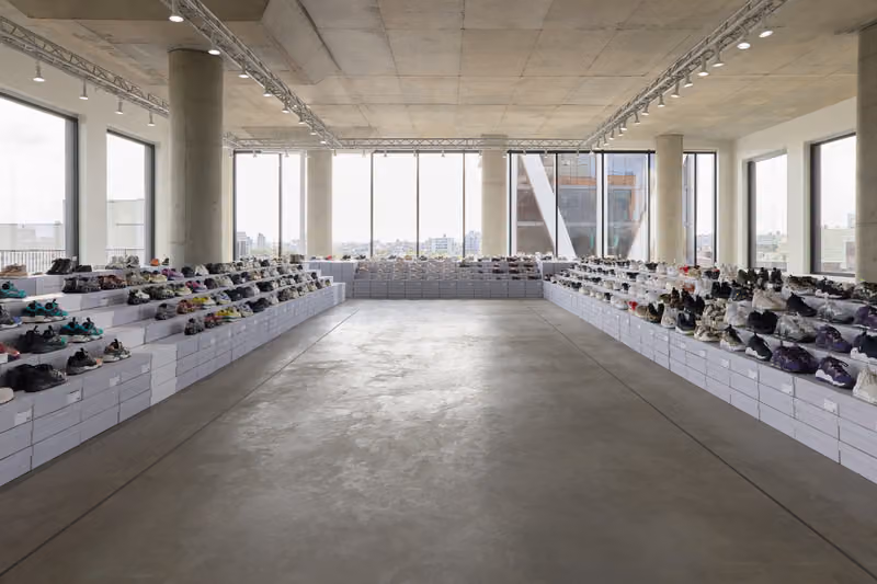 Bright Kith archive room with rows of shoes displayed on low white shelves beside tall windows