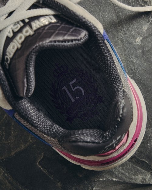 Tongue detail showing dark 15th anniversary crest, pink midsole edge visible, New Balance 990v3