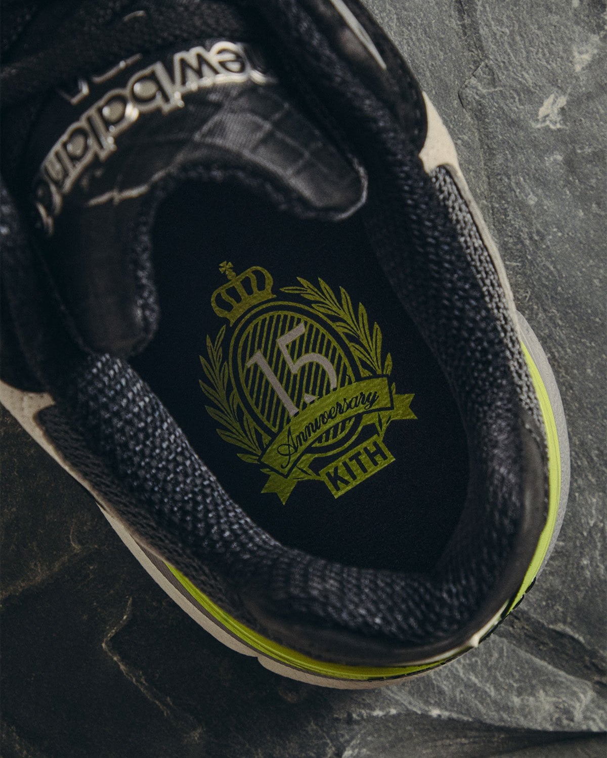 Tongue detail showing olive 15th anniversary Kith crest on black lining, New Balance 990v3
