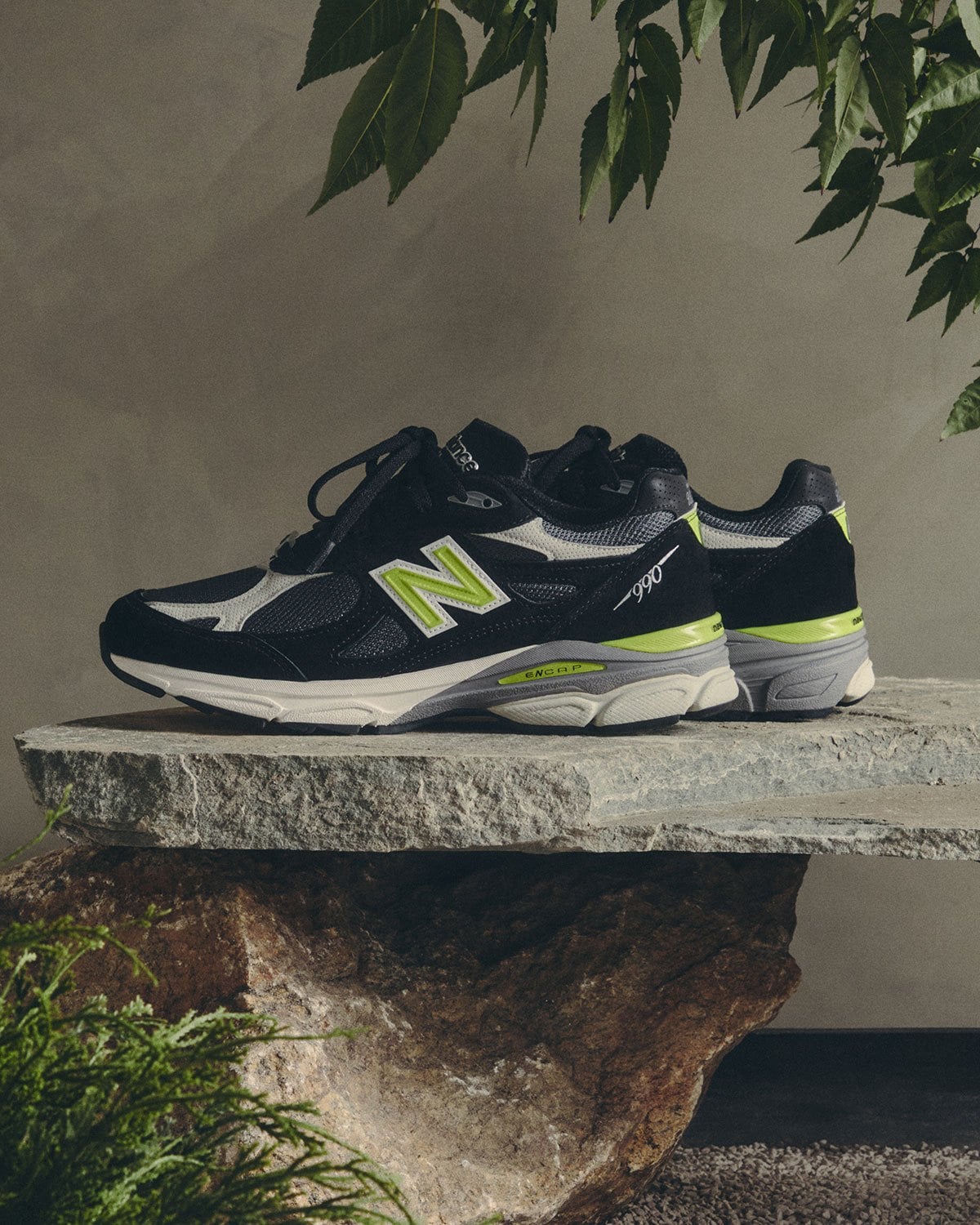 Lateral view, black suede with lime green N logo, under green leaves, New Balance 990v3