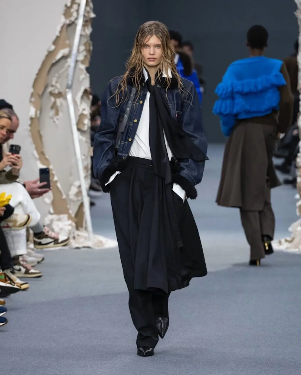 runway, black shearling collar jacket over black wide trousers, front row seated, Sacai FW26 Collection