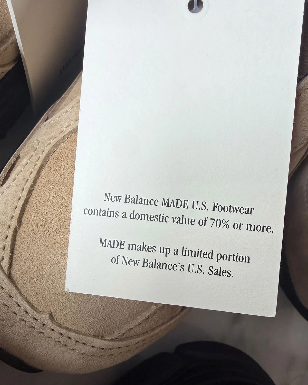 detail shot of hangtag reading 'New Balance MADE U.S. Footwear' over tan suede, Tan Suede