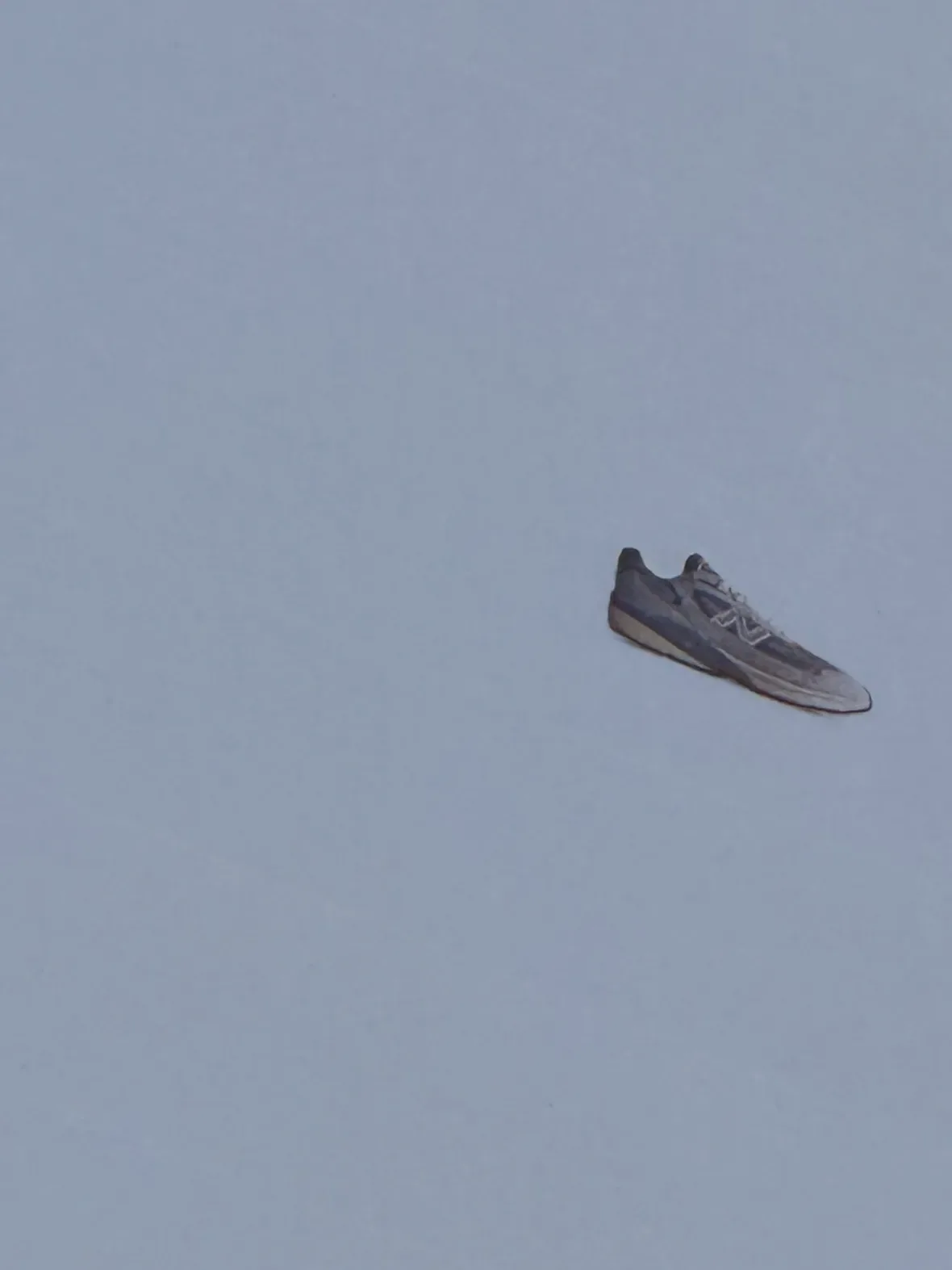 lateral view, grey-and-white upper with N logo, floating against grey sky, New Balance 990v7