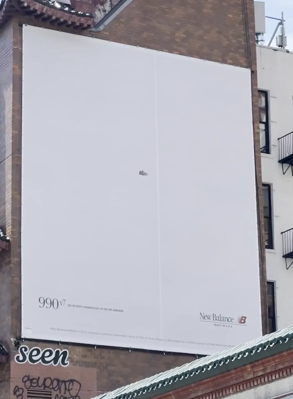 billboard on brick building reading 990v7 and New Balance, graffiti tag below, New Balance 990v7