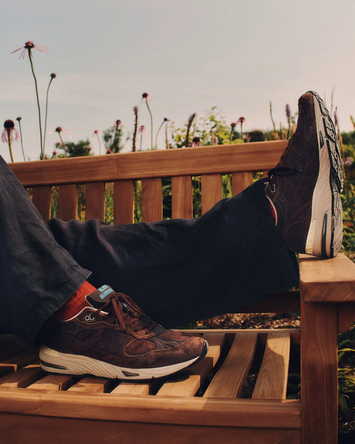 on-foot, propped on wooden bench with red socks and wildflowers behind, x Bleue Burnham