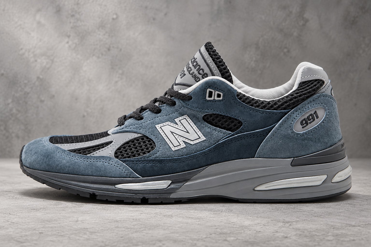 lateral view, slate blue suede with black mesh panels and silver N logo, concrete, New Balance 991v2 “Elevated Essentials”