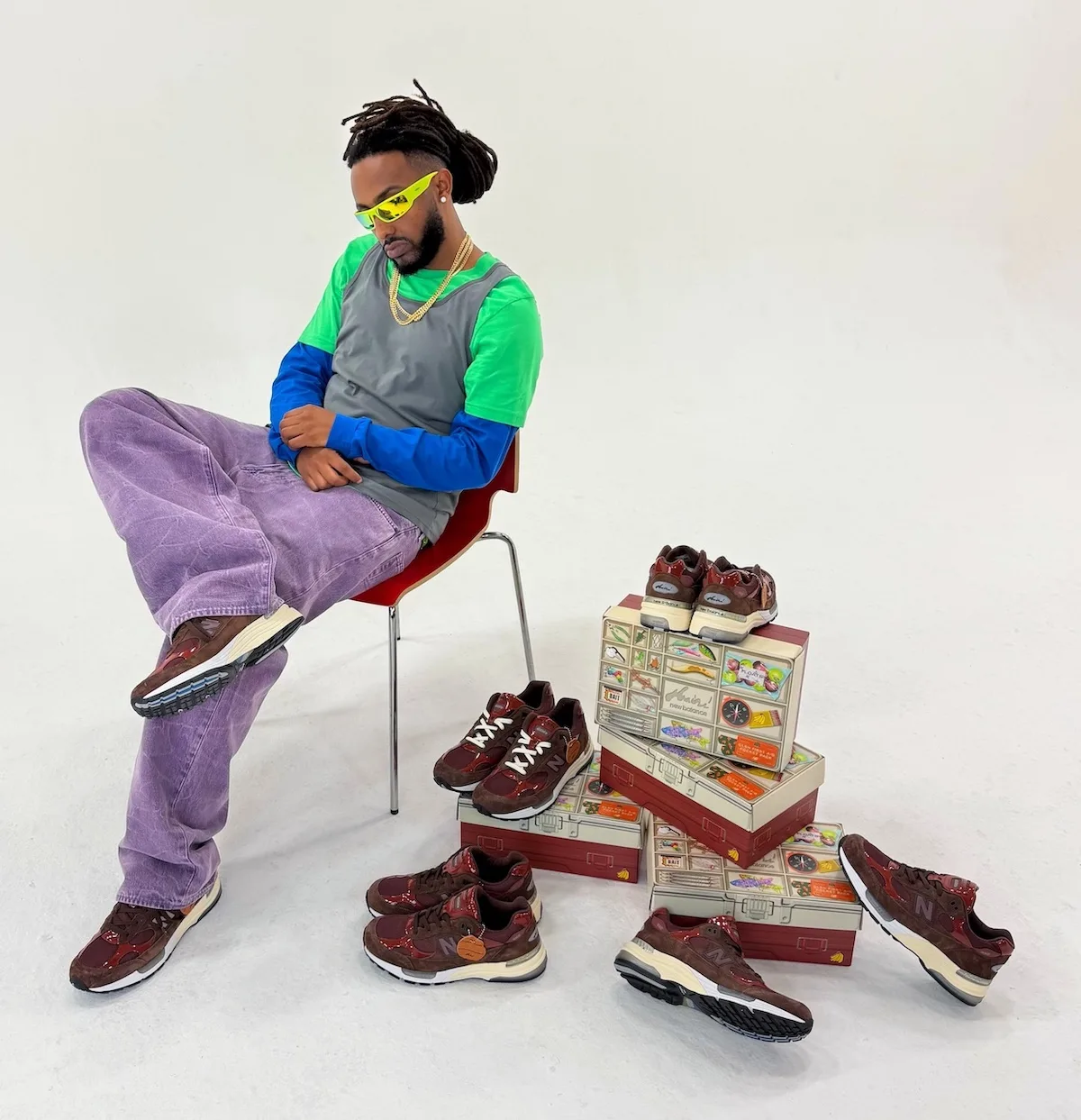 seated model beside stacked tackle-box packaging and three pairs of sneakers, Outdoor School
