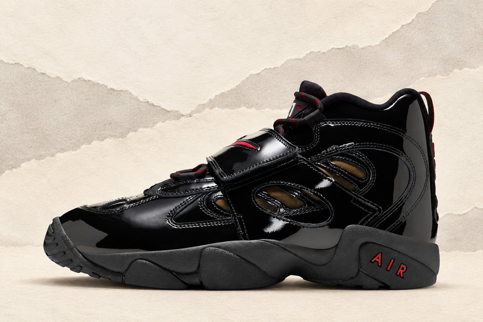 lateral view on textured tan backdrop, black patent leather with red swoosh strap, Nike Air Diamond Turf 2 “Black Patent”