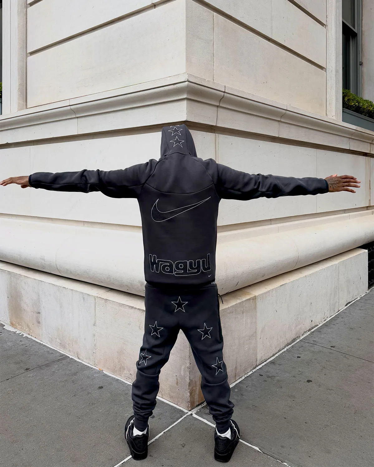 on-foot rear view, black hoodie with reflective wagyu text and star-print sweatpants, 90 x Wagyu
