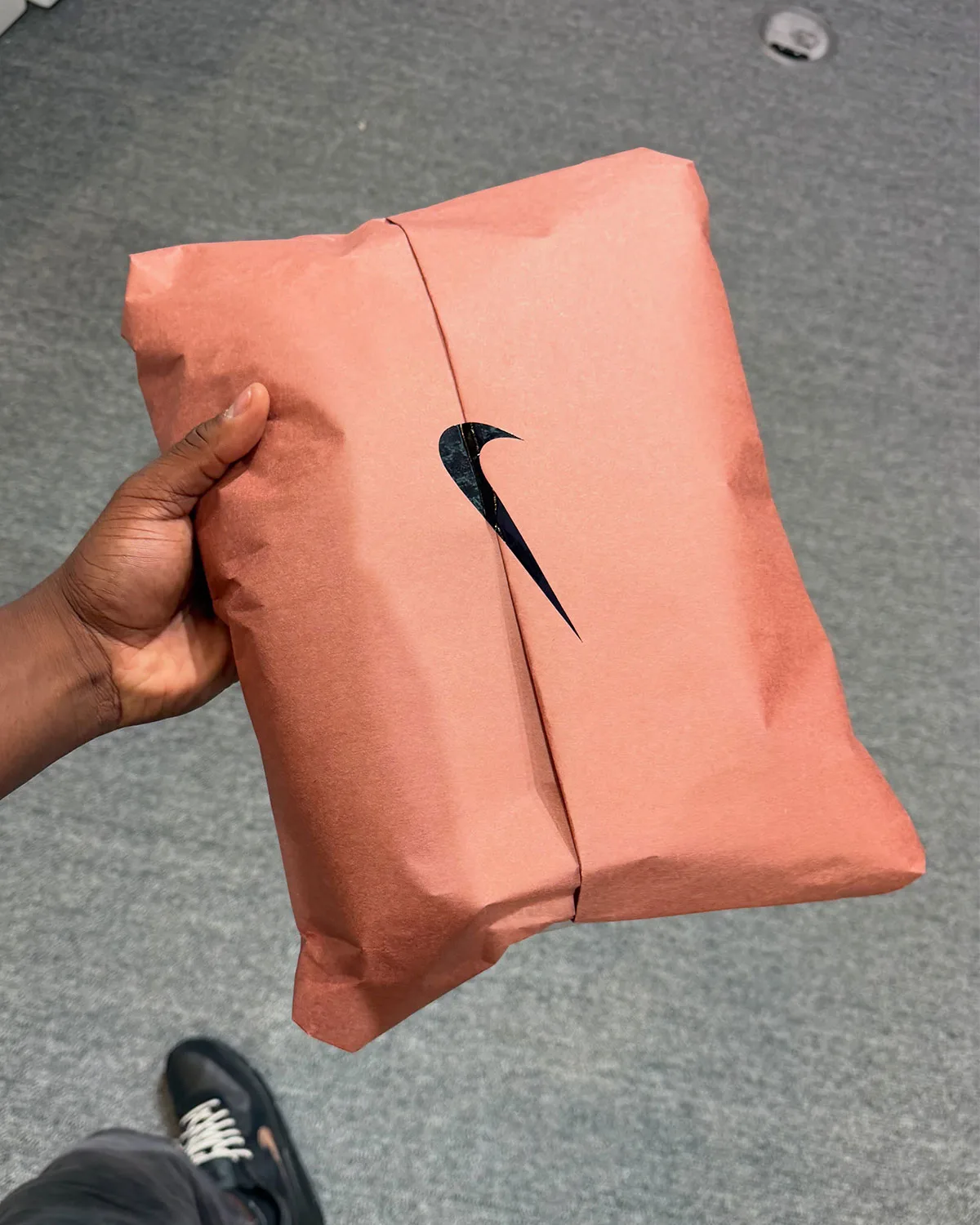in-hand wrapped box detail, coral paper with die-cut swoosh window revealing black shoe, 90 x Wagyu