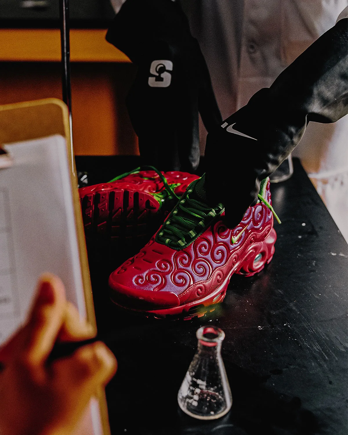 pair on dark tabletop, red swirl uppers with green laces beside a glass flask, Ope Ope