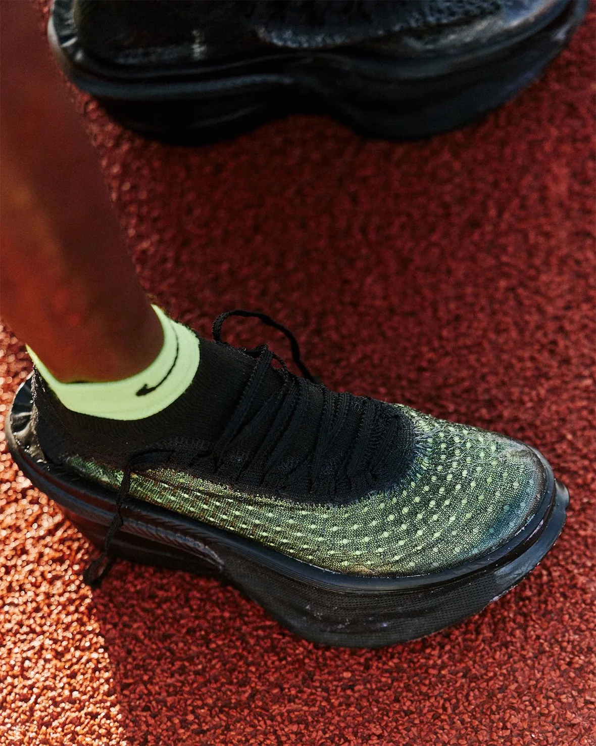 on-foot close-up, iridescent green and black upper with black sock on red track, Nike Apex